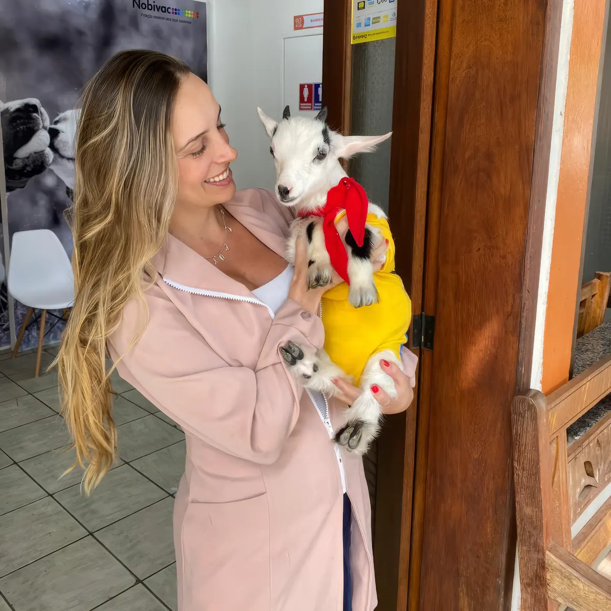 Dra. Luana, fundadora do Vet do Pet, segurando um cabrito filhote com uma roupa amarela e vermelha.